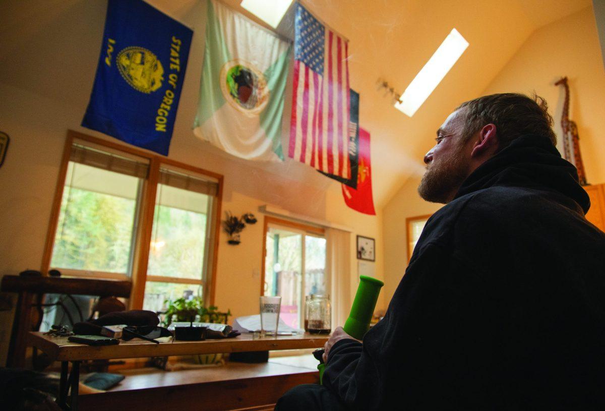 Jeremiah Civil exhales smoke Friday, March 22, 2019, at his home near Estacada. The flags, left to right, are those of the state of Oregon; U.S. Department of the Interior; United States; prisoners of war and service members missing in action; and the U.S. Marine Corps. "These are the cults I've belonged to," he said.